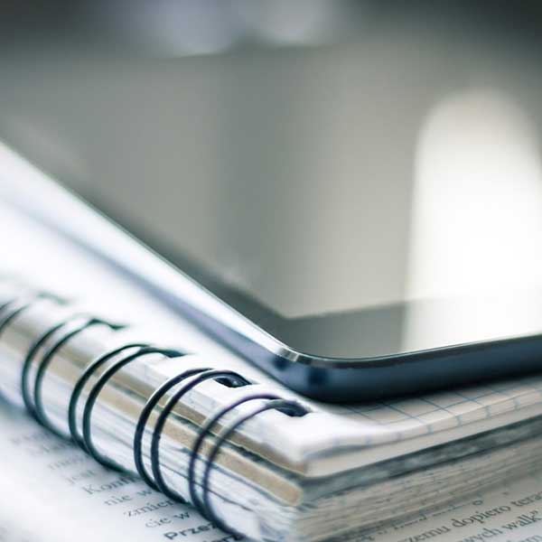 une tablette posée sur un cahier à spirale pour réviser son Master Journalisme sportif de l'IICP